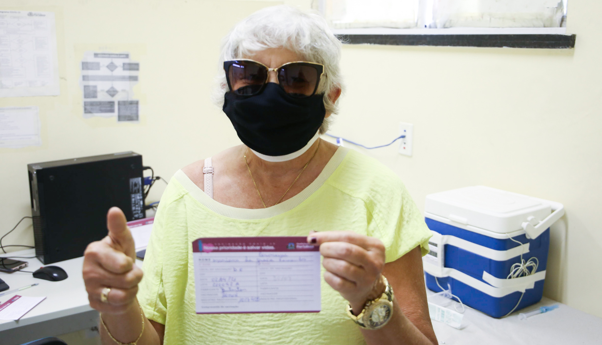 senhora de máscara mostra seu cartão de vacinação